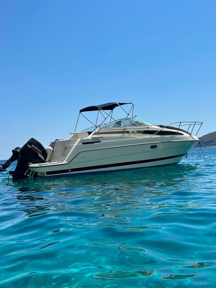 ΝΙΚΟΛΑΟΣ, the MareWaves cabin cruiser, anchored in clear turquoise water off Zakynthos, with a blue bimini top and a Suzuki outboard engine
