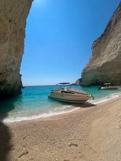 The MareWaves boat framed by a natural cave arch on a pebble beach in Zakynthos