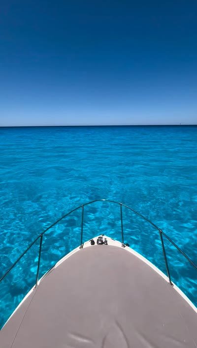 The bow of the boat pointing across clear shallow water toward the open horizon
