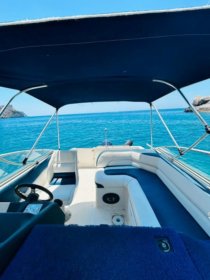 The cockpit of ΝΙΚΟΛΑΟΣ from the stern step, showing the navy floor mat, the helm seat and the bench seating under the bimini