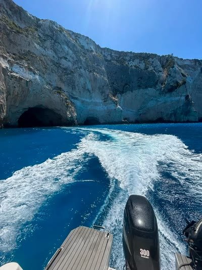 The boat's wake curving away from dark cave mouths cut into the pale cliffs at the northern tip of Zakynthos
