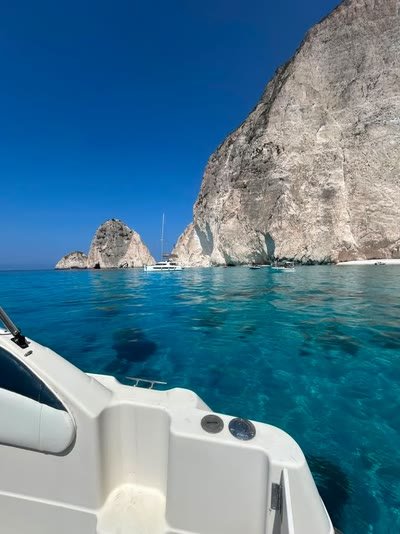 Deep blue water below the sheer white cliffs of the Zakynthos west coast, a catamaran anchored in the distance
