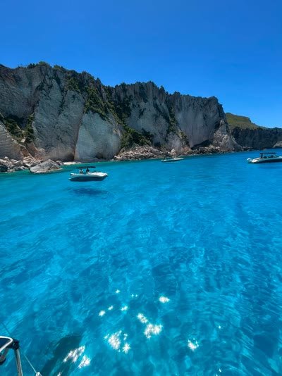 Pale white cliffs dropping into brilliant blue water on the Keri coast, with small boats anchored close in