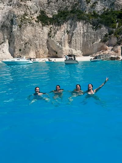 Four friends swimming together in vivid blue water below the cliffs