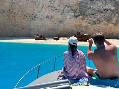 A couple sitting on the bow of the boat photographing the Navagio shipwreck