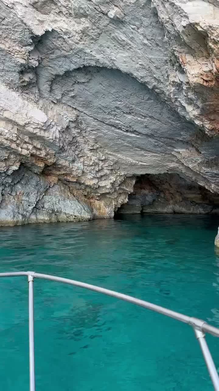 The MareWaves boat gliding right up against a huge overhanging sea cave on the Zakynthos west coast, emerald water below the bow