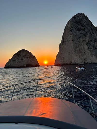 The sun setting exactly in the gap between the two Mizithres sea stacks, seen over the bow of the boat
